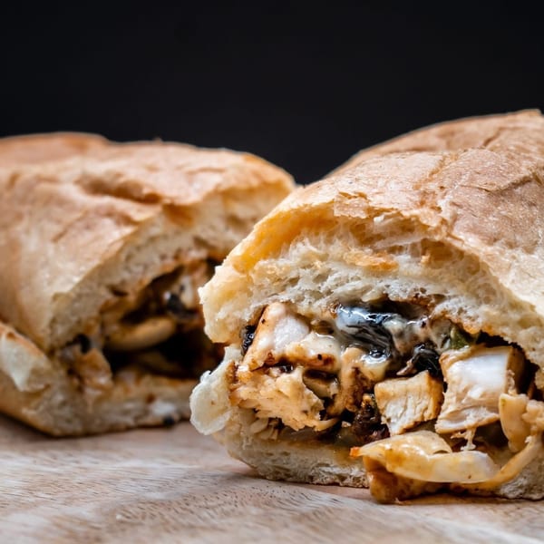 Two halves of a chicken and cheese sub sandwich on a wooden cutting board.