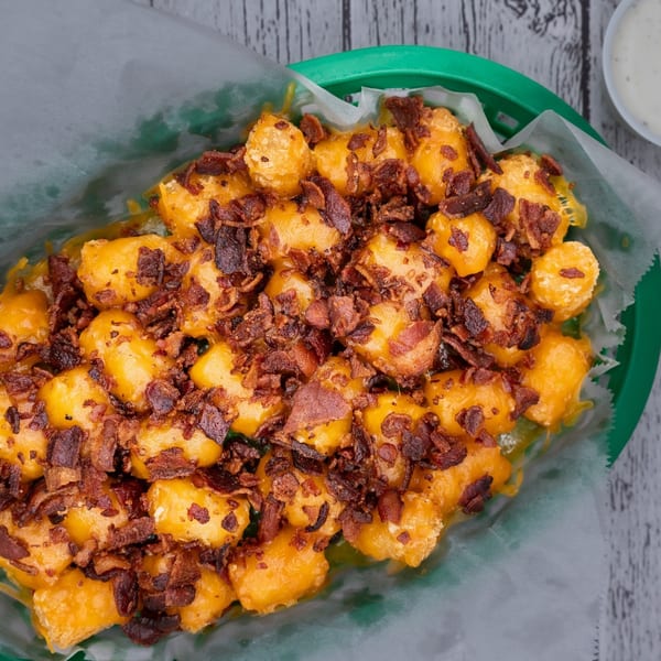 Loaded tater tots with melted cheese and crispy bacon bits in a green basket with ranch.